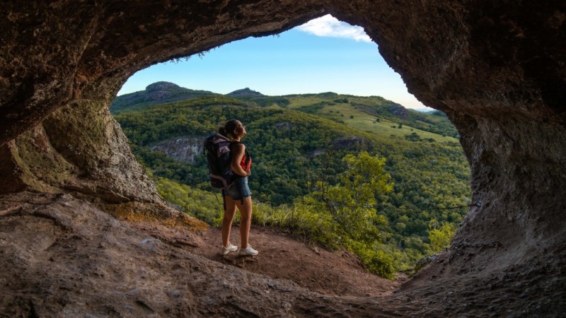 Mulher na entrada de Caverna apreciando a vista campestre do lado externo